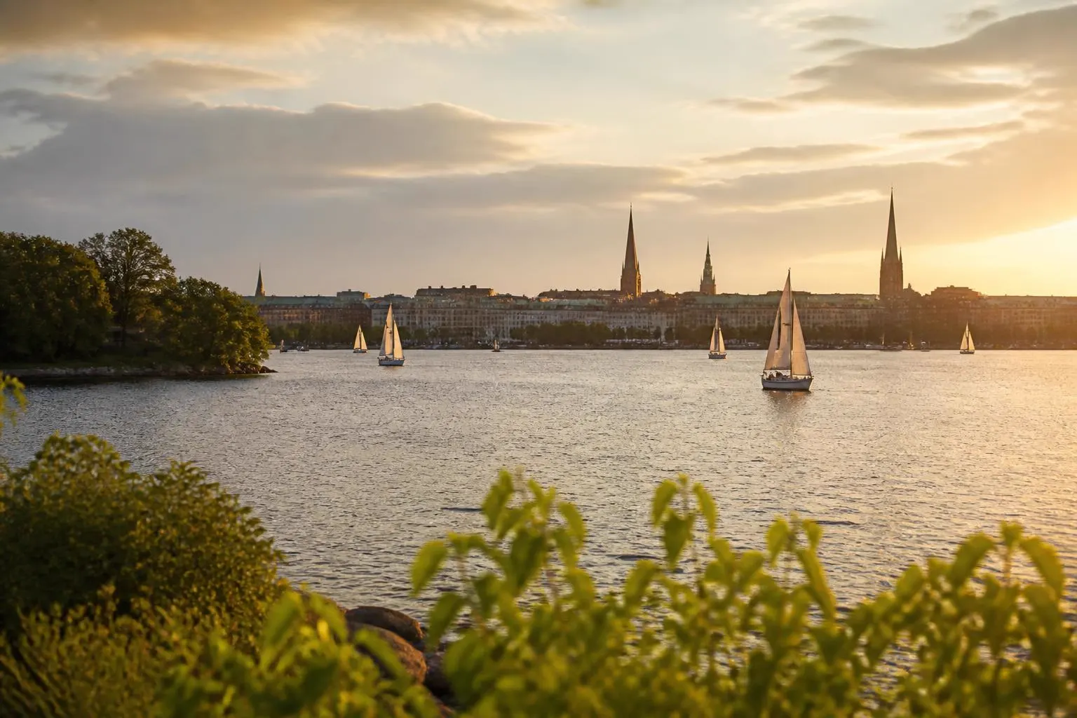 Weites Binnengewässer mit Segelbooten, dahinter eine Stadtsilhouette mit Kirchtürmen