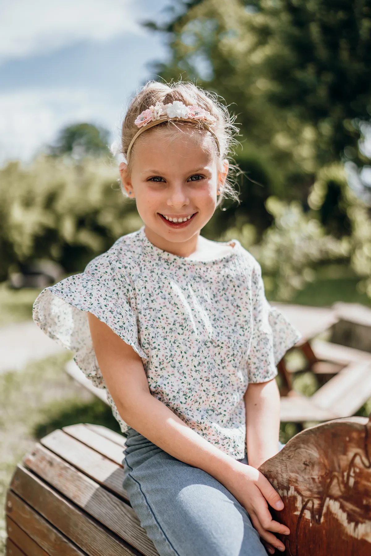 Kindergartenfoto: Blondes Mädchen sitzt lachend auf einem Holzpferd im Kita-Garten