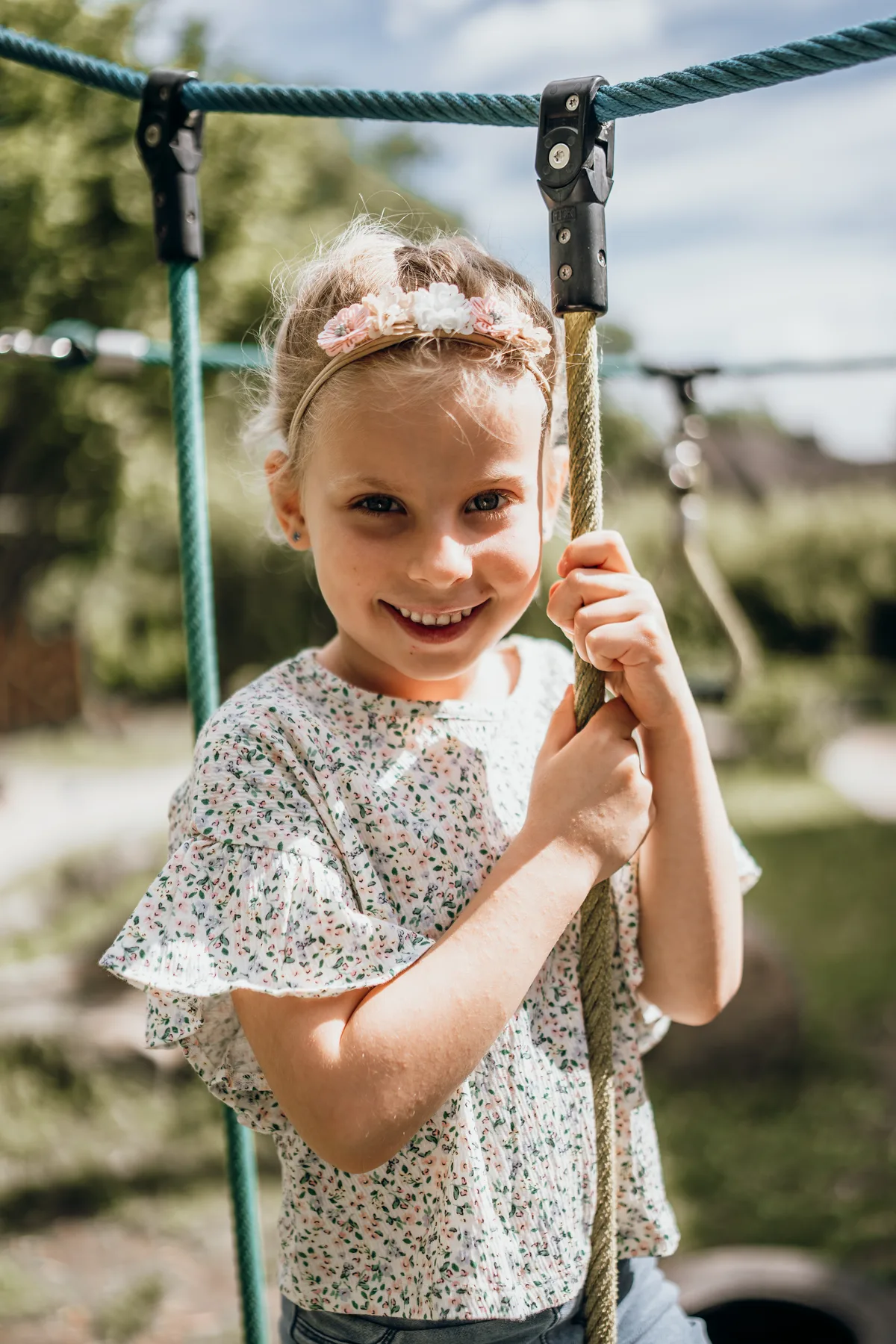 Kindergartenfoto: Mädchen hält sich am Kletterseil fest und lacht in die Kamera