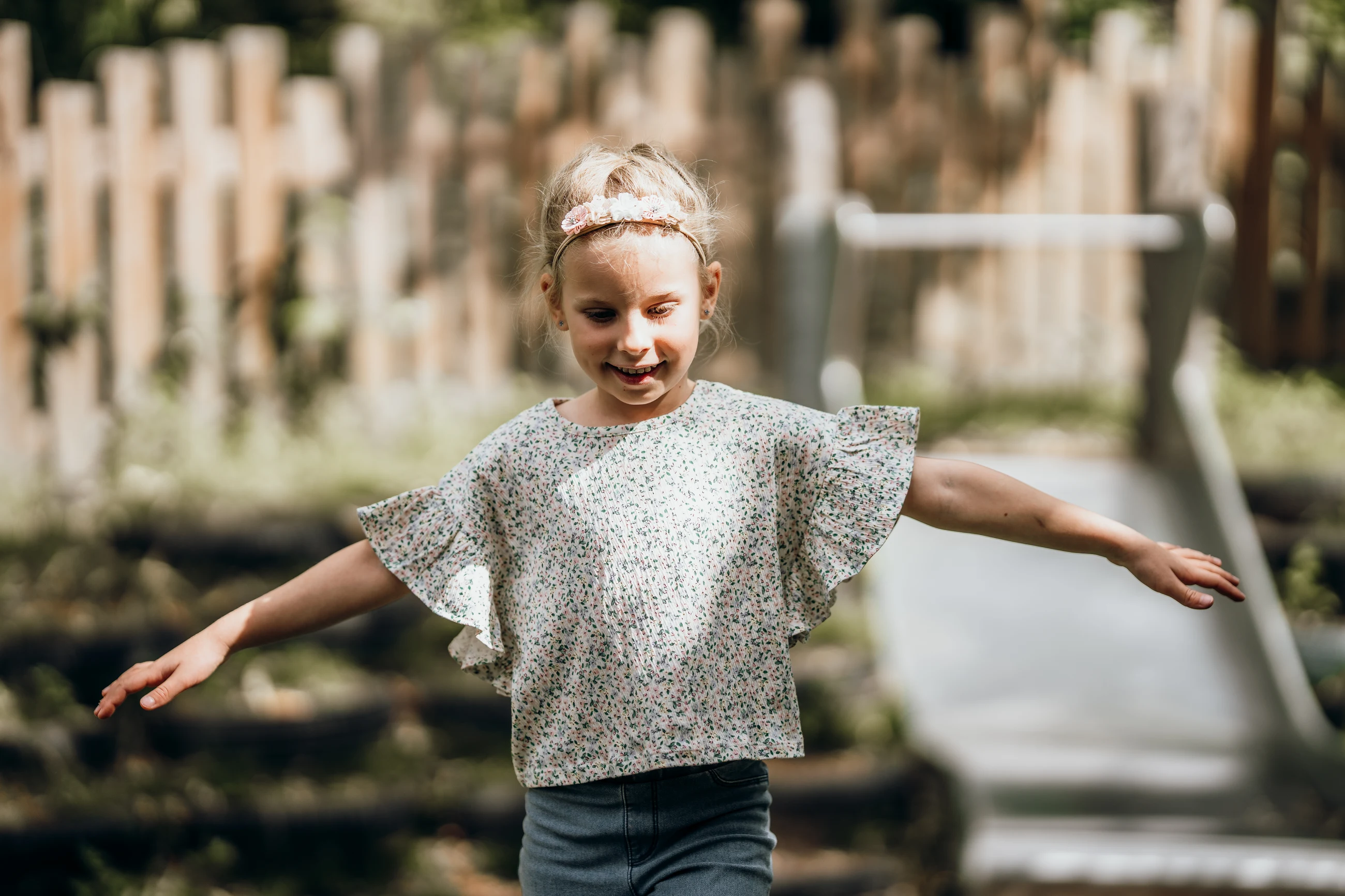 Kita-Fotografie: Mädchen läuft mit ausgebreiteten Armen über den Spielplatz