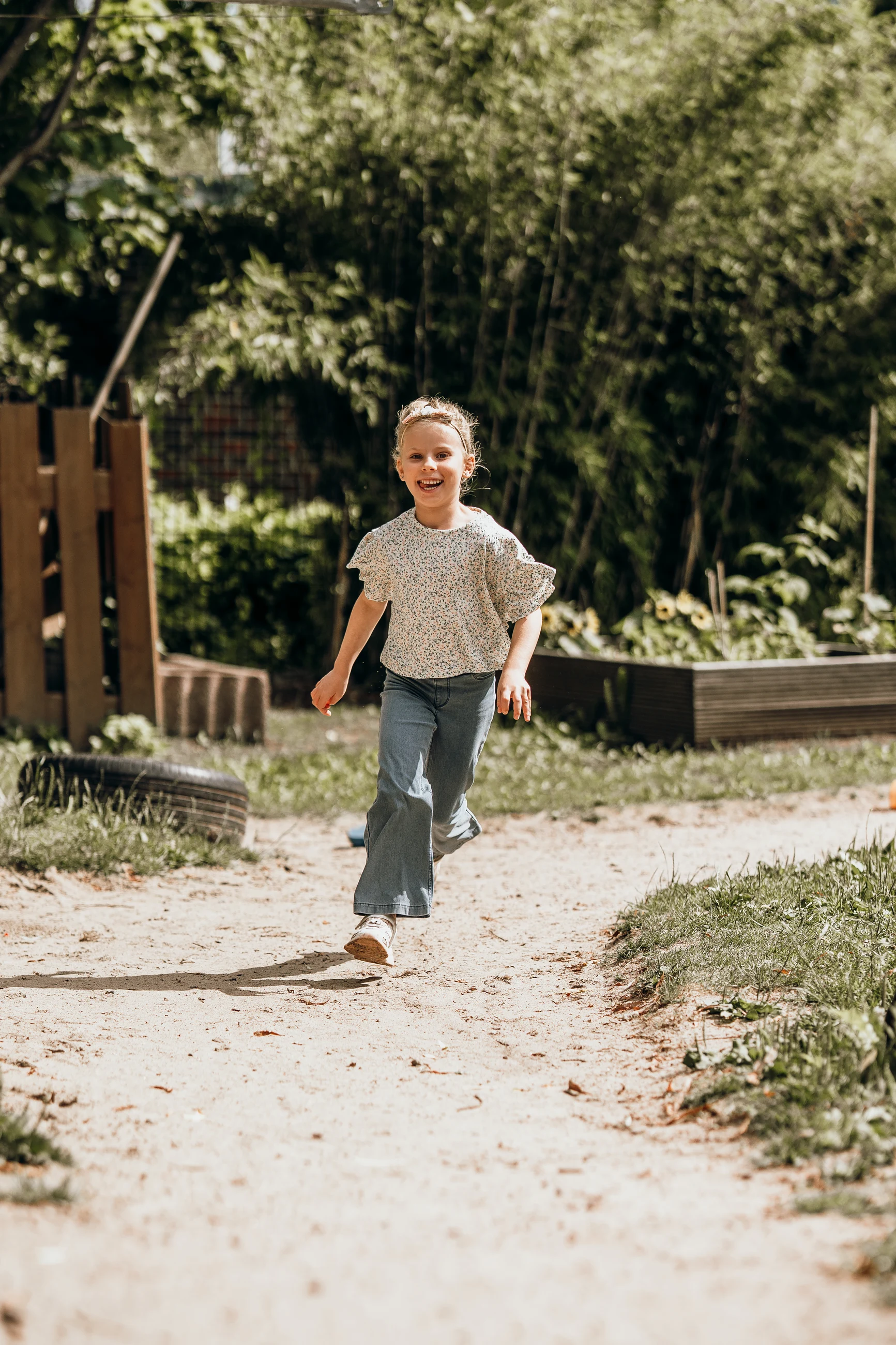 Kindergartenfotografie: Mädchen rennt lachend über einen Sandweg auf die Kamera zu