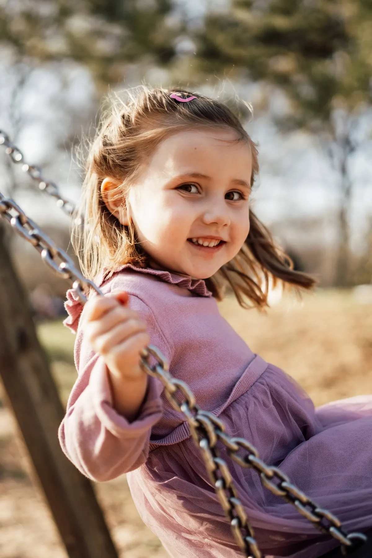 Kindergartenfotografie: Mädchen im lila Kleid schaukelt im warmen Abendlicht
