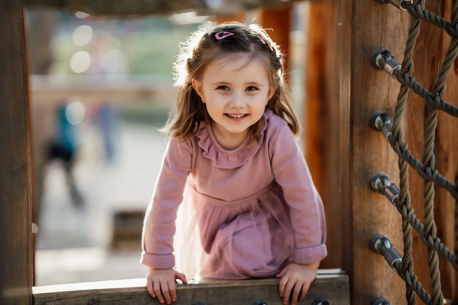 Kindergartenfoto: Mädchen schaut lachend aus einem hölzernen Klettergerüst