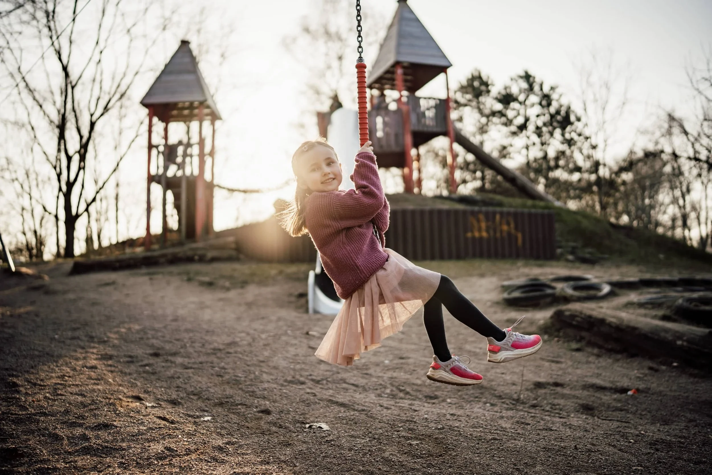 Kindergartenfoto: Kind schwingt im Gegenlicht vor einem hölzernen Spielturm