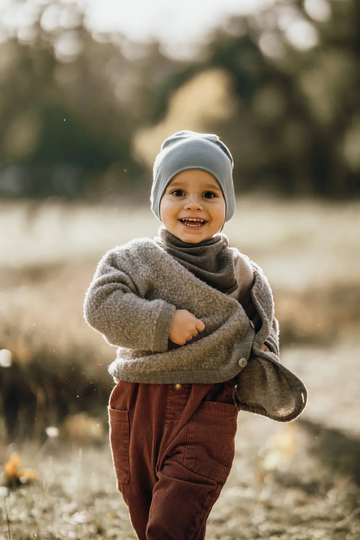 Kindergartenfoto: Kleinkind mit Mütze läuft lachend über ein herbstliches Feld
