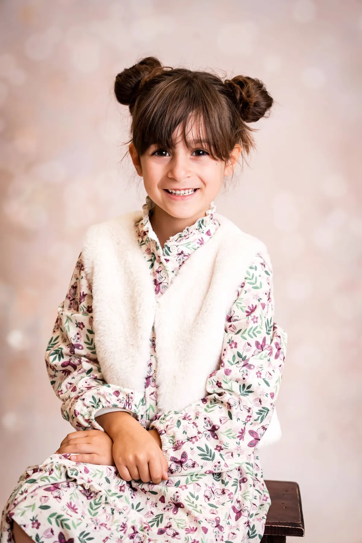 Grundschul-Porträt: Mädchen mit Duttfrisur und Blumenkleid schaut freundlich in die Kamera