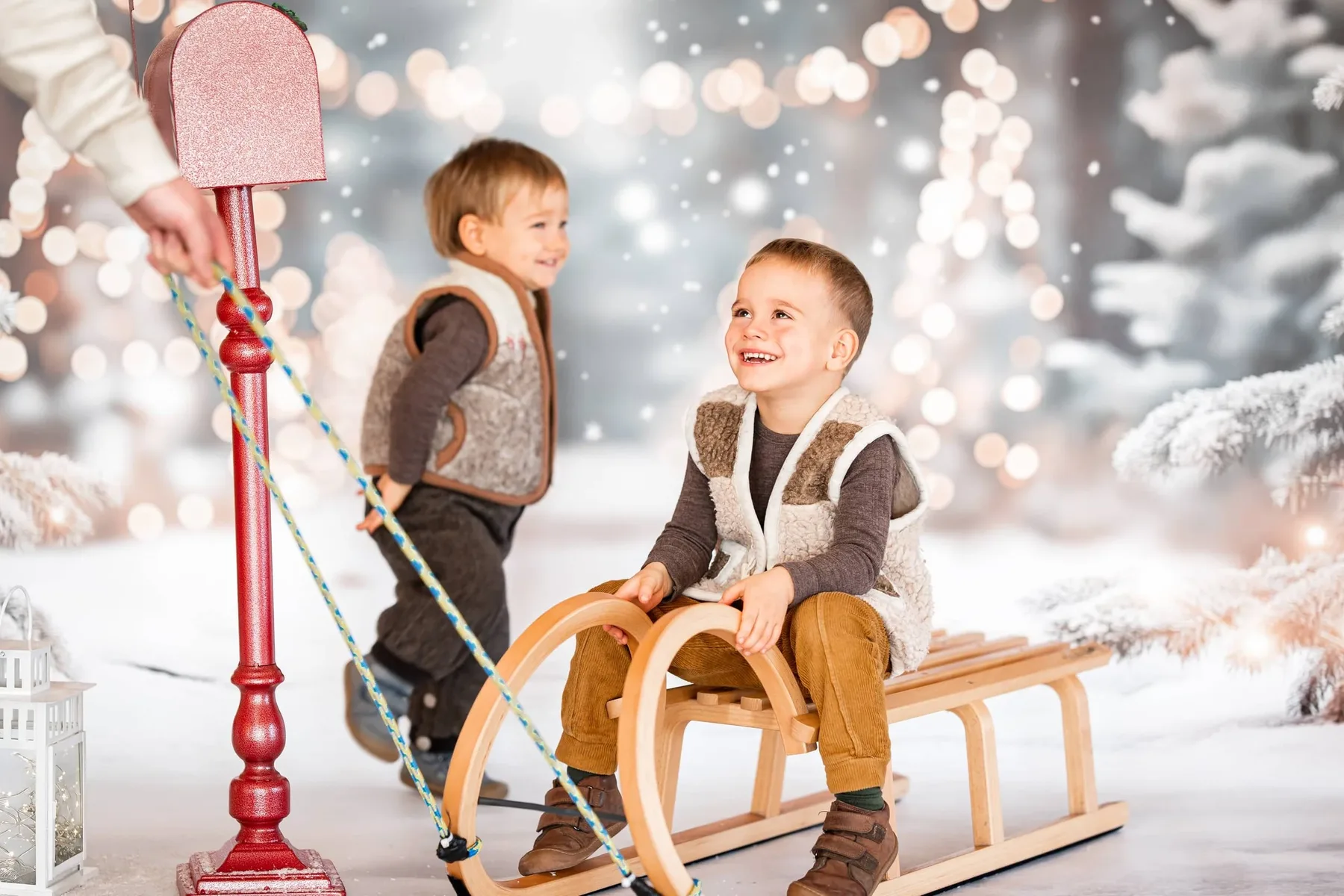 Kinderfotografie: Zwei Jungen mit Holzschlitten lachen im weihnachtlichen Winterset