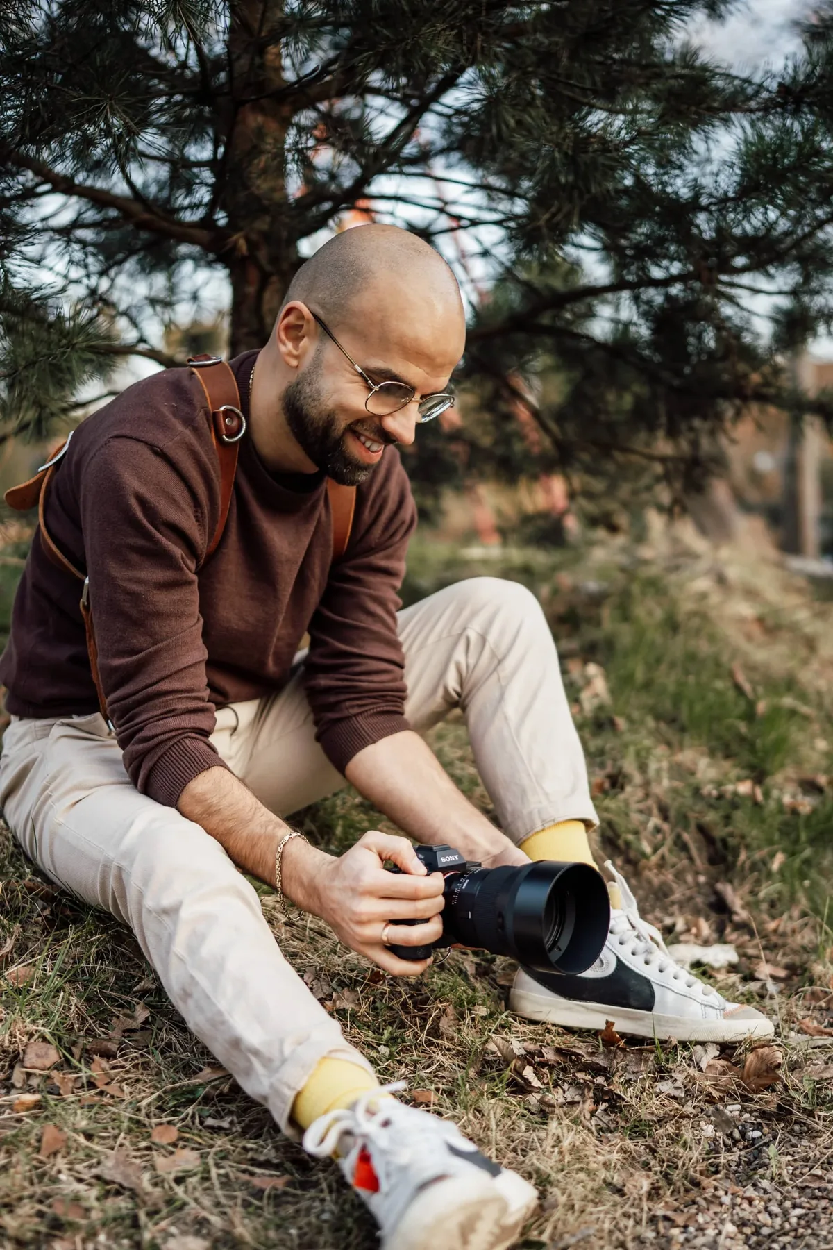 Fotograf sitzt am Boden zwischen Bäumen und wechselt das Objektiv