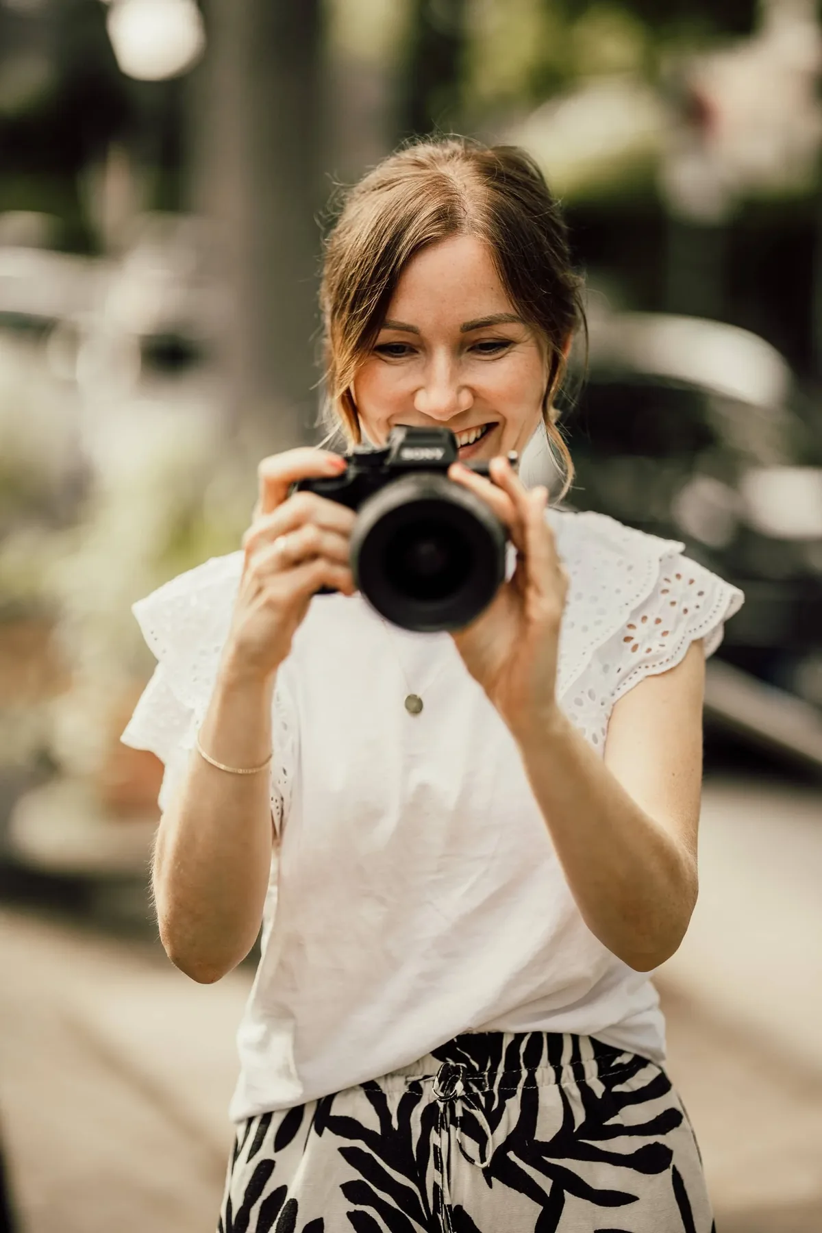 Fotografin in weißer Bluse fotografiert lächelnd im Freien