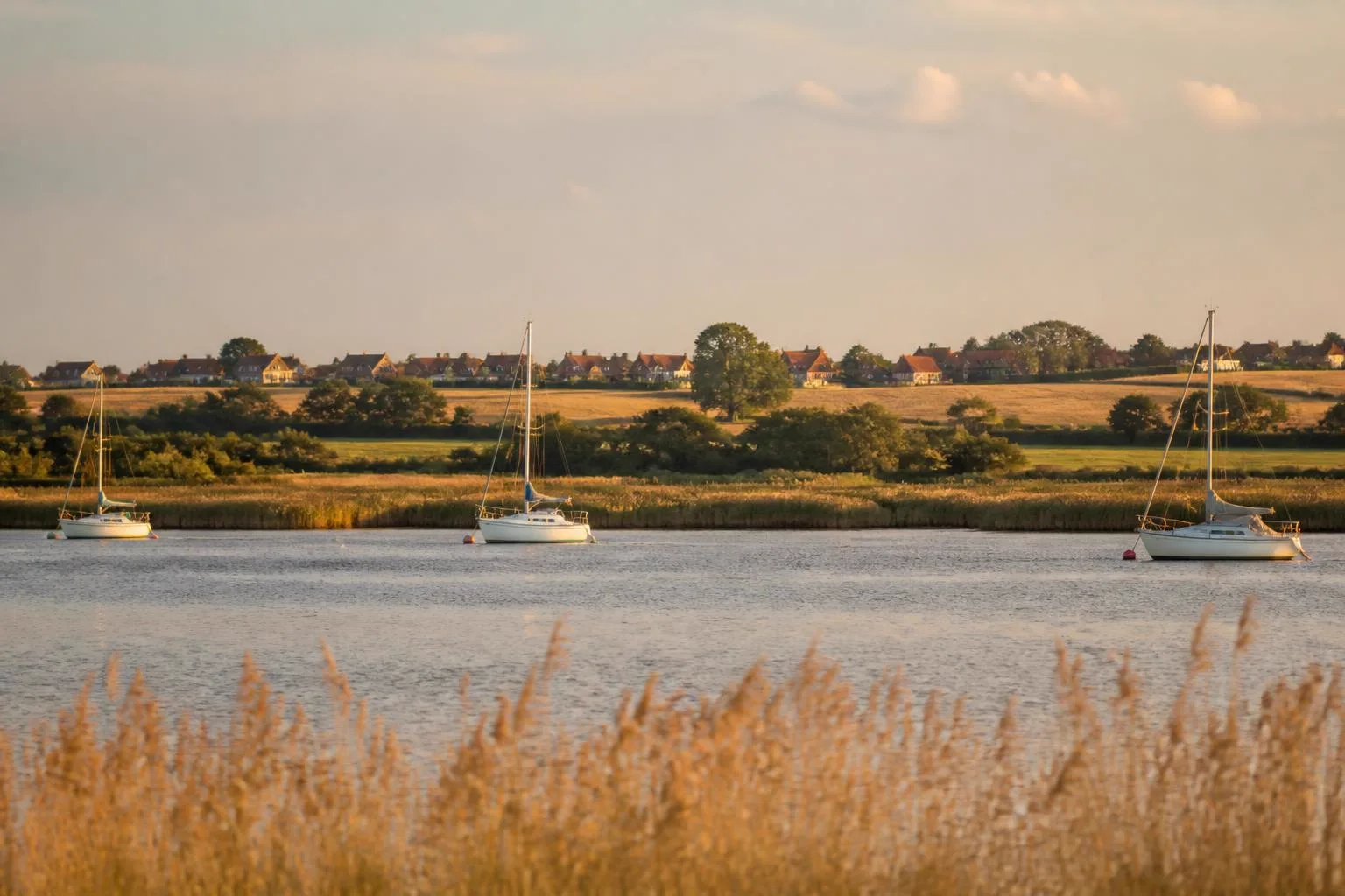Flache Bucht mit ankernden Segelbooten, dahinter Hügelland und ein Dorf mit roten Dächern