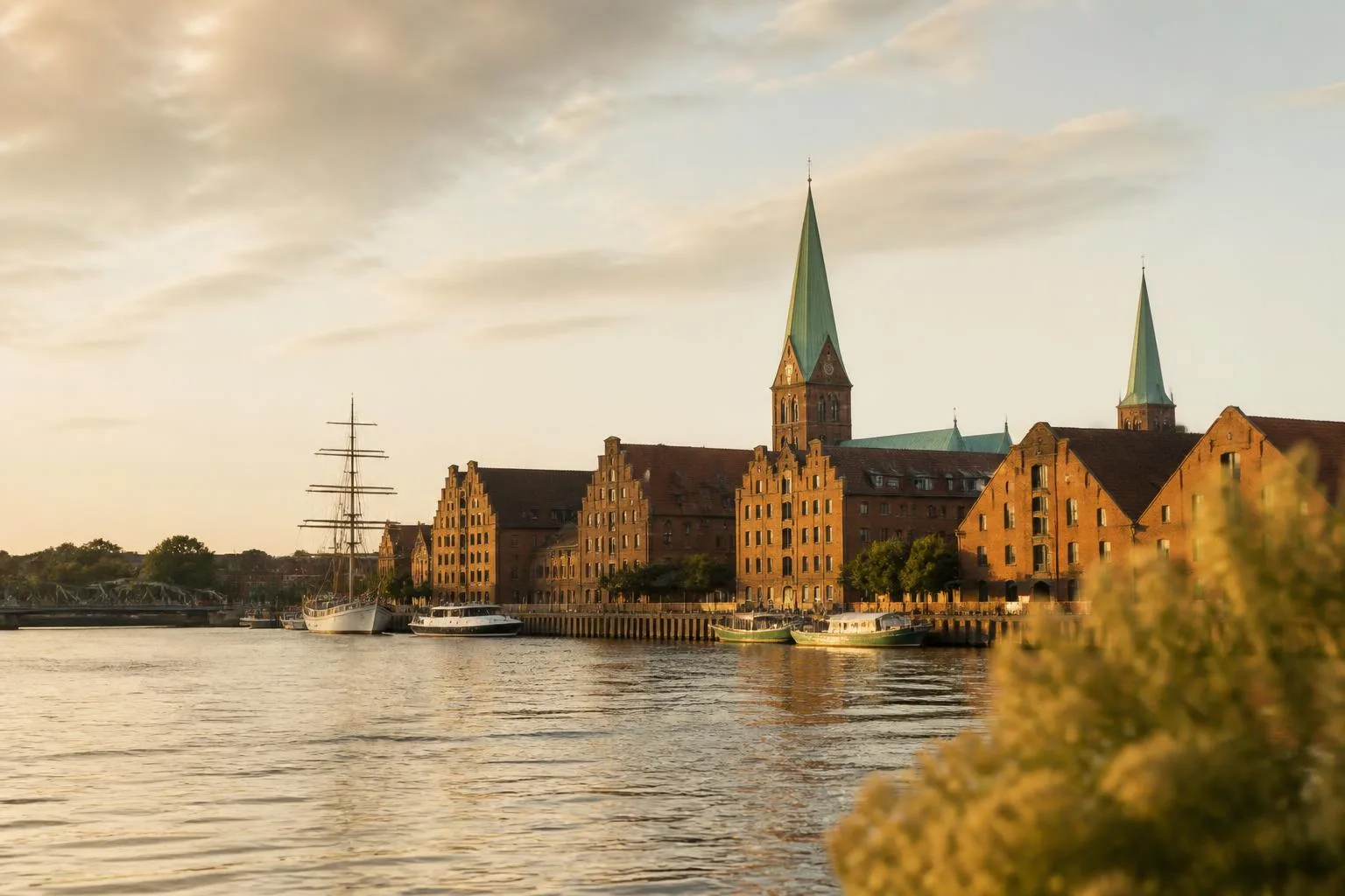 Backsteinspeicher und Kirchtürme am Stadthafen, davor Masten und kleine Boote am Kai