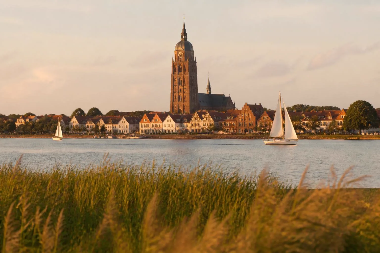Backsteinkirche mit hohem Turm über niedrigen Häusern an einer weiten flachen Bucht