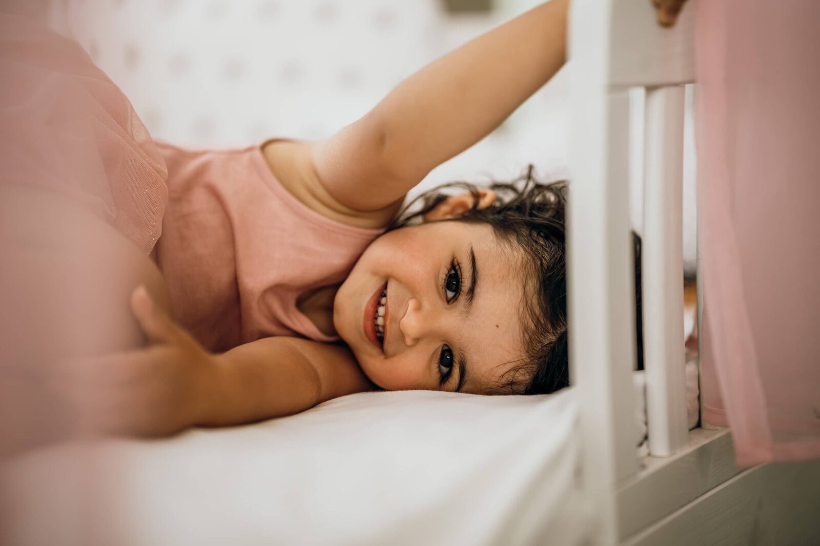 Kinderporträt: Kind liegt lachend auf dem Bett und schaut in die Kamera