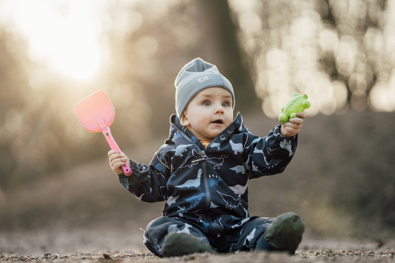 Kindergartenfoto: Kleines Kind sitzt mit Sandschaufel im Sand, Gegenlicht am späten Nachmittag