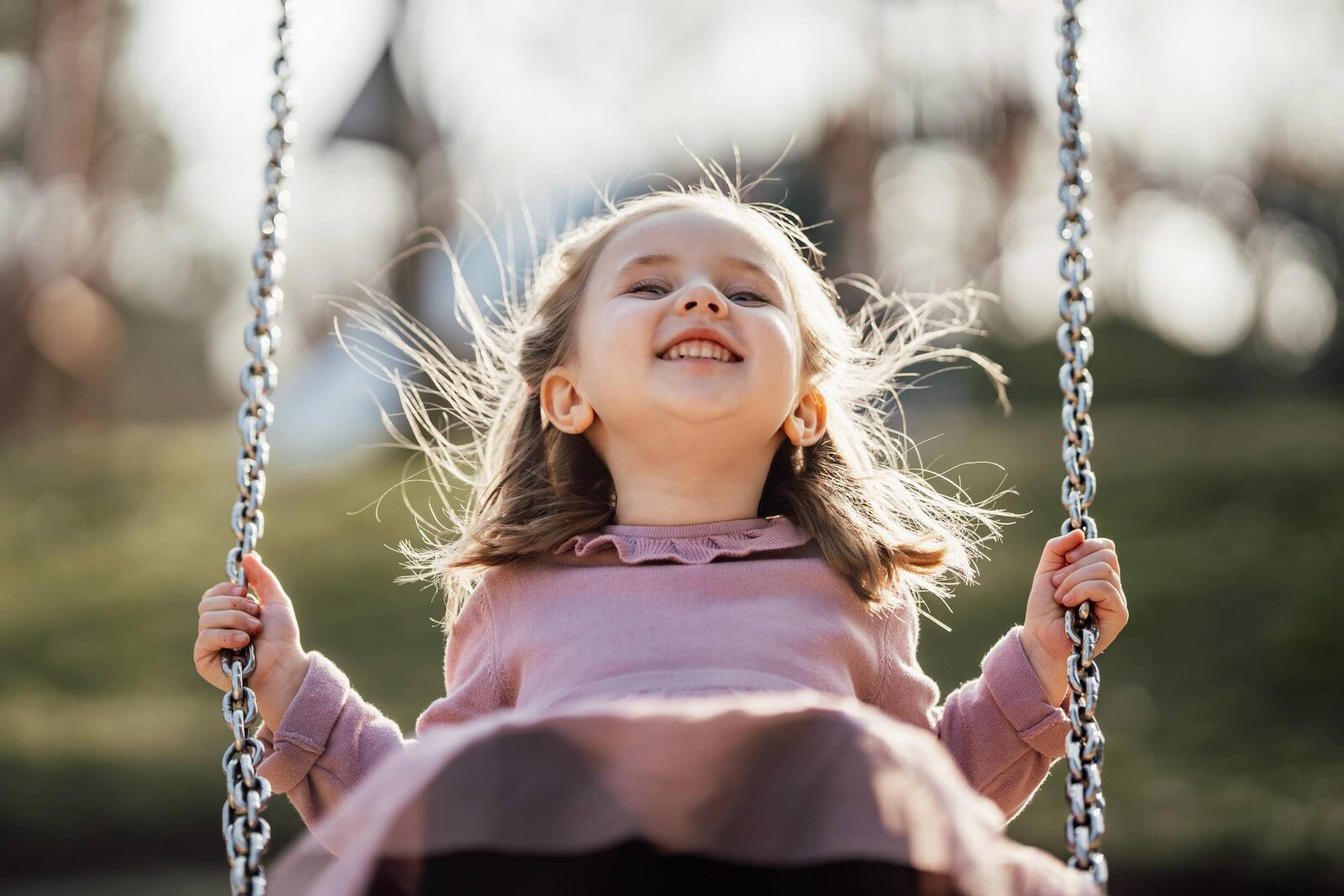 Kita-Fotografie: Mädchen schaukelt und lacht mit fliegenden Haaren auf dem Spielplatz
