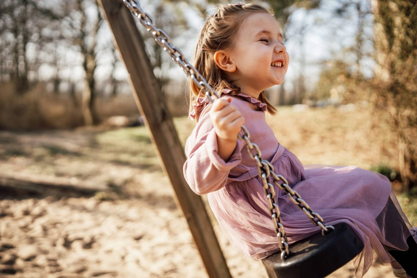Kindergartenfotografie: Mädchen auf der Schaukel im Profil, warmes Abendlicht auf dem Sandplatz