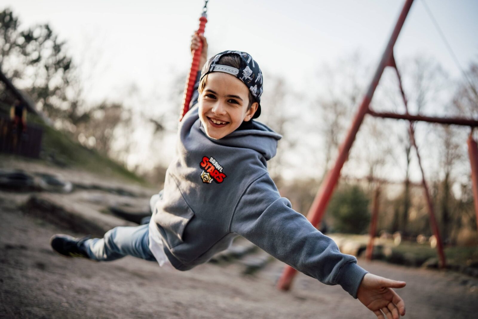 Kindergartenfoto: Junge mit Cap streckt lachend den Arm aus, während er auf der Schaukel sitzt