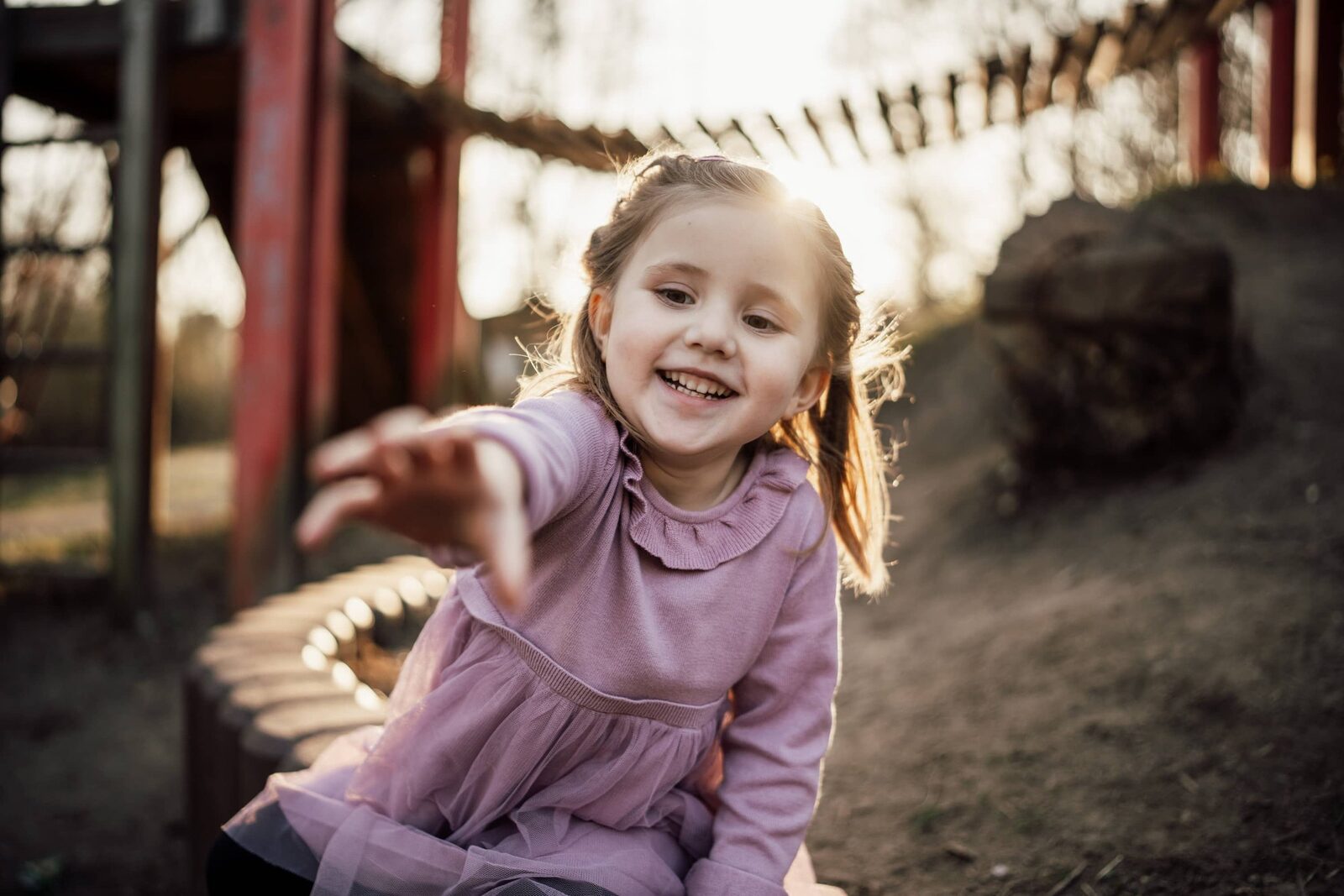 Kita-Fotografie: Mädchen sitzt auf dem Spielgerät und streckt die Hand in Richtung Kamera