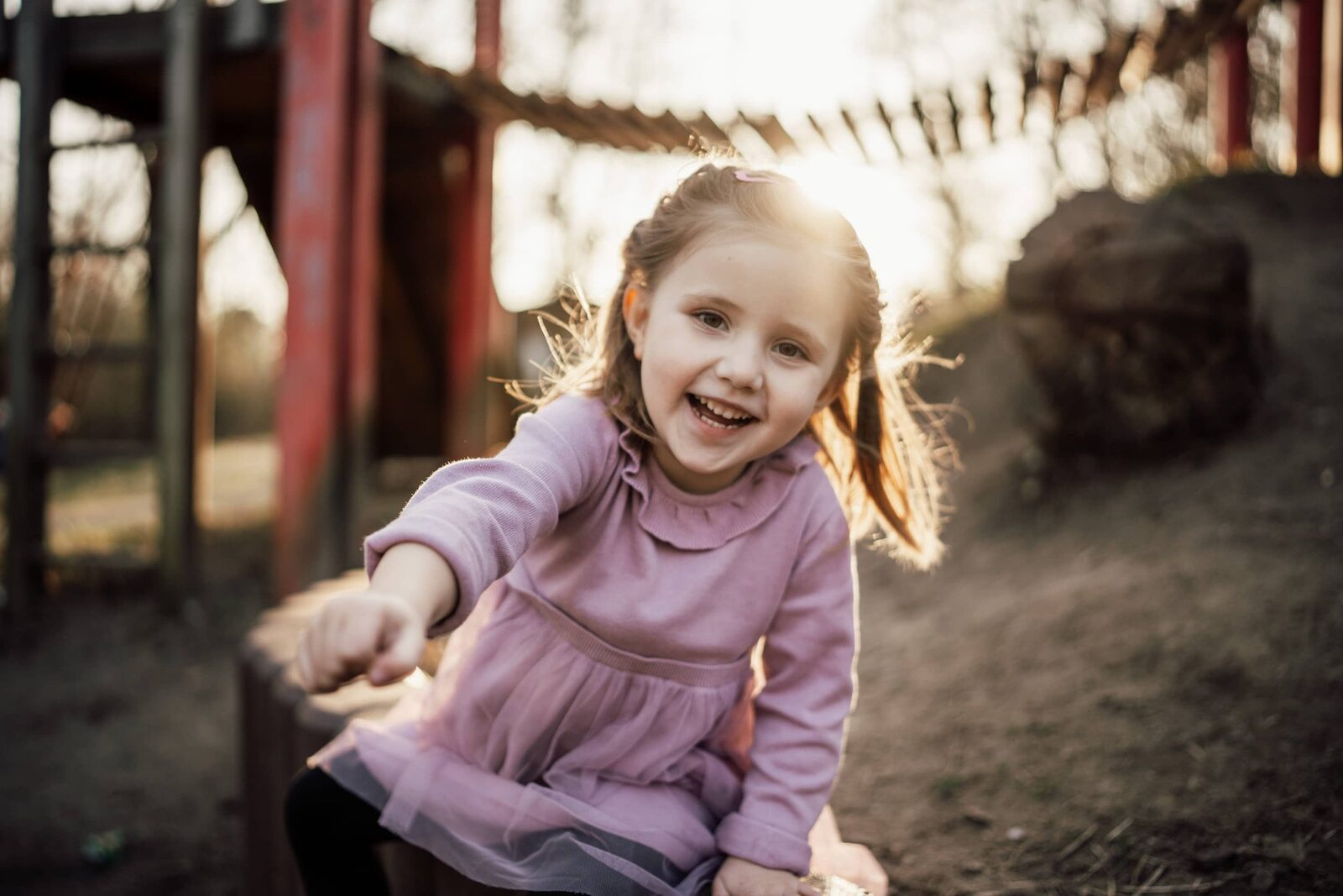 Kindergartenfotografie: Lachendes Mädchen auf dem Spielplatz, weicher Hintergrund im Sonnenlicht