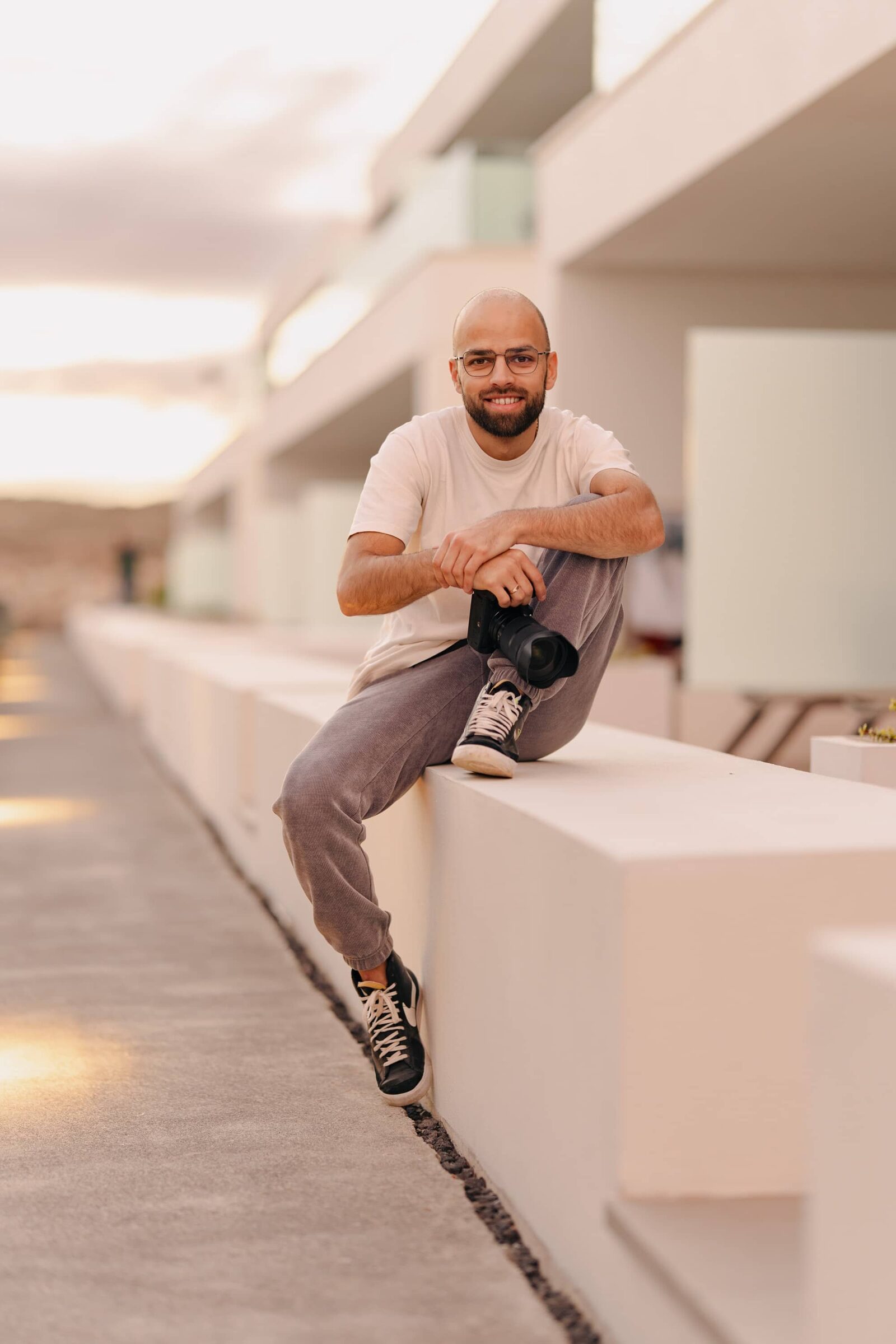 Serkan Can sitzt mit der Kamera in der Hand auf einer hellen Mauer