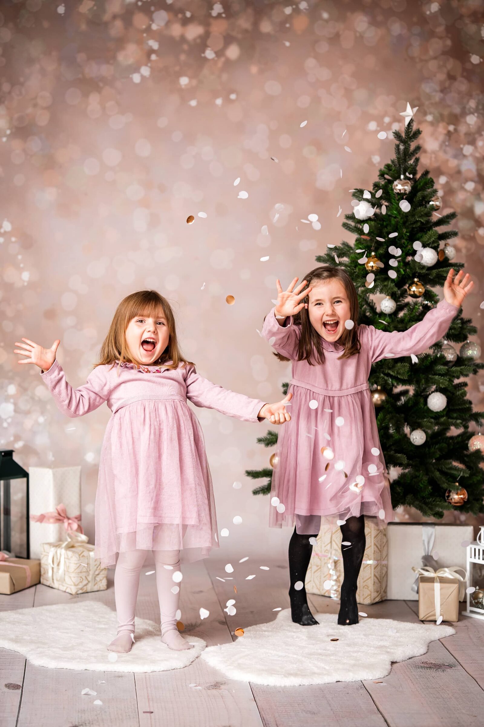 Kinderfotografie: Zwei Mädchen jubeln im Weihnachts-Set vor dem geschmückten Baum